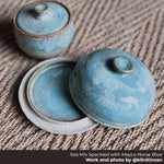 Two lidded bowls made from Seattle Pottery Supply sea mix speckled clay and norse blue glaze on a woven surface