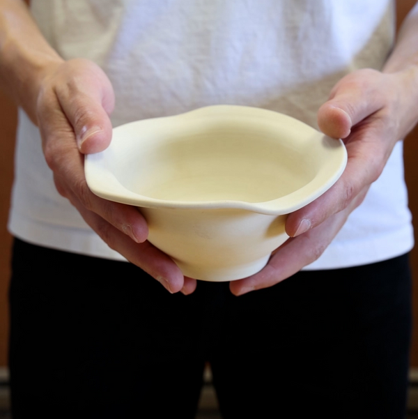 A bowl with a rippled rim, help by two hands. Made out of Seattle Freeze Mid-Range Translucent Porcelain